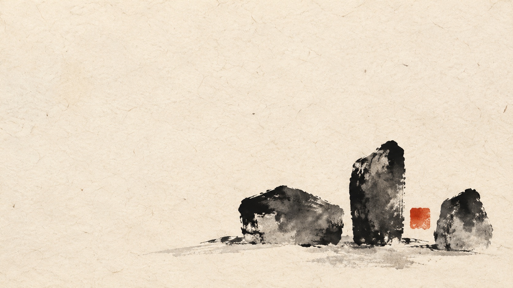 Three irregular charcoal inkstone forms and a small vermilion square sit near the lower-right edge of warm ivory washi paper, leaving broad empty space across the left.