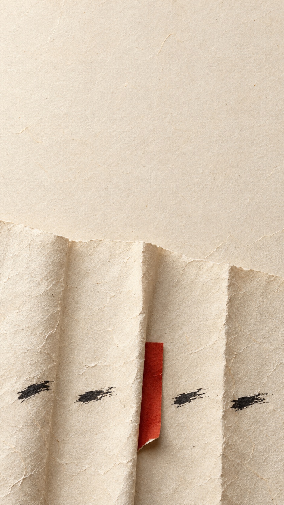 Folded warm cream washi paper forms three shallow vertical ridges with sparse black sumi brush marks and one narrow vermilion paper strip near the lower third.